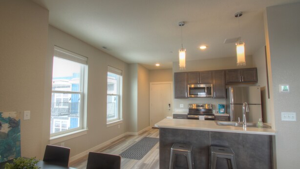 A modern kitchen with stainless steel appliances, a central island with stools, and large windows providing natural light. - 2 bedroom + 1 bath apartment with amazing views! (Missoula)