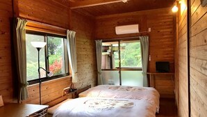 A wooden cabin room with a bed, a desk, a lamp, and a TV. - Yakushima Shikinoyado Onoaida (Yakushima)