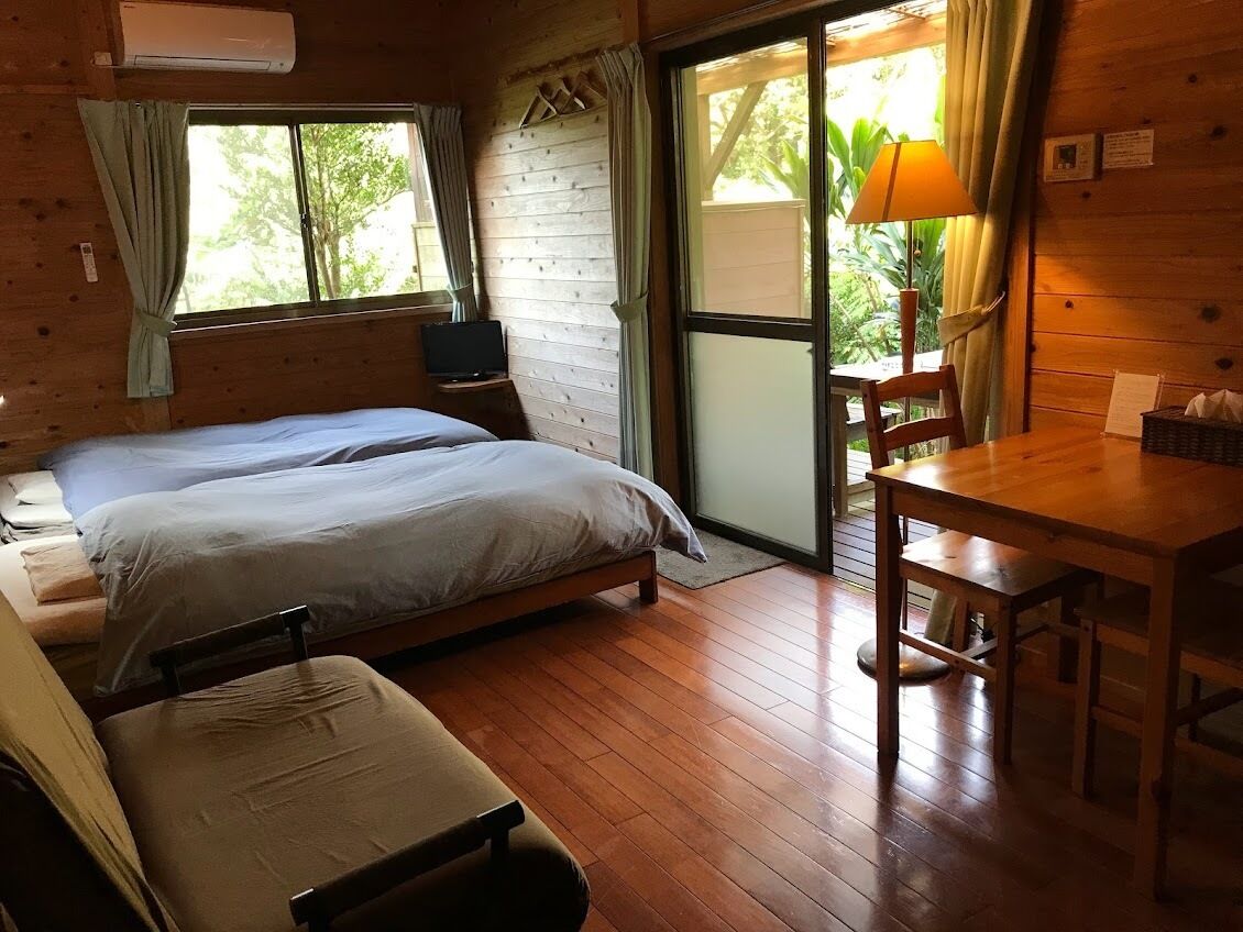 A wooden cabin room with a bed, a table, and a chair.