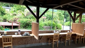 A covered outdoor seating area with wooden tables and chairs, a concrete floor, and a view of lush greenery. - Yakushima Shikinoyado Onoaida (Yakushima)