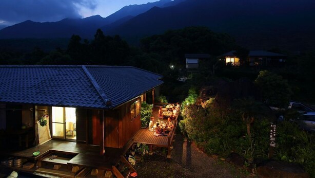 A wooden house with a tiled roof, a deck, and a dining area with people. - Yakushima Shikinoyado Onoaida (Yakushima)