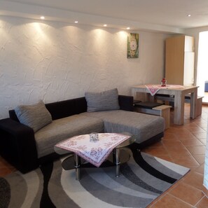 A modern living room with a sectional sofa, a small table with a decorative table runner, and a wall clock. - Vacation apartment Untersberg 38sqm (Berchtesgaden)