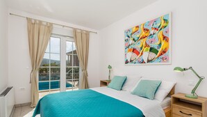 Ein Schlafzimmer mit einem großen Bett, Blick auf einen Swimmingpool und einem farbenfrohen, abstrakten Gemälde an der Wand.