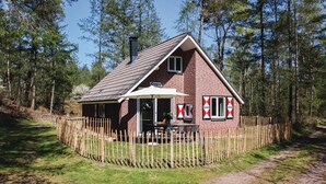 Ein kleines Backsteinhaus mit Satteldach, Holzzaun und einer Terrasse mit Sitzgelegenheit im Freien.