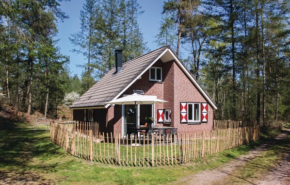 A small brick house with a sloped roof, a wooden fence, and a patio area with outdoor seating.