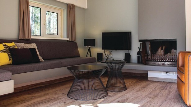 Ein Wohnzimmer mit einer Couch, zwei schwarzen Tischchen, einem Fernseher und einem Kamin.