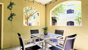 A dining area with a table and chairs, a decorative plant, and views of buildings through arched windows. - Amazing main floor resort style condo at Avalon (Clearwater)