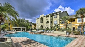 A swimming pool with lounge chairs, a covered area, and a multi-story building with balconies. - Amazing main floor resort style condo at Avalon (Clearwater)