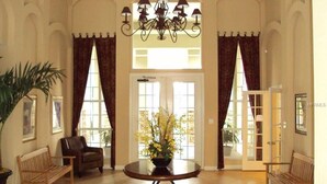 A spacious lobby with a round table, two chairs, a chandelier, and a large window with curtains. - Amazing main floor resort style condo at Avalon (Clearwater)