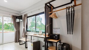 A modern hotel room with a large window, a desk with a kettle, a radio, and a suitcase. - Monotel Aonang (Krabi)