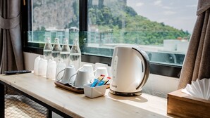 A hotel room with a view of a mountainous landscape, a ZAGIO electric kettle, several white mugs, and a tray with a cup holder and a box of tissues. - Monotel Aonang (Krabi)