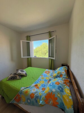 Un dormitorio con una cama, una ventana con cortinas y vistas a árboles desde el exterior.