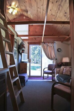 Interior acolhedor de uma cabana com teto de madeira, escada, sofá, poltrona e televisão sobre um suporte de madeira.