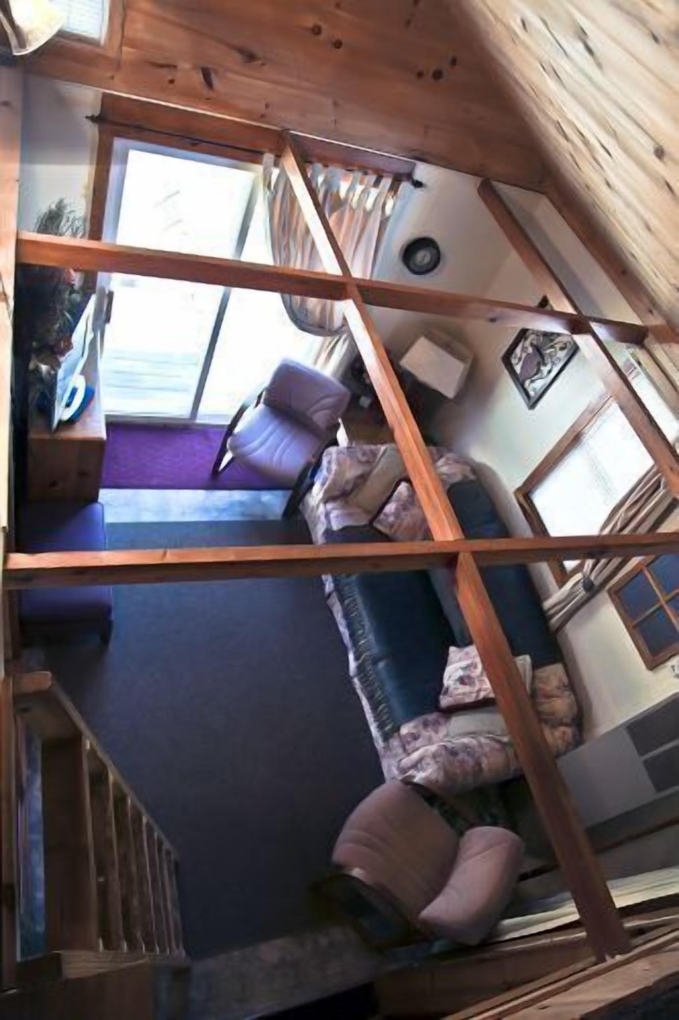 Interior de una cabaña con techo de madera, un sofá, un sillón y una ventana.