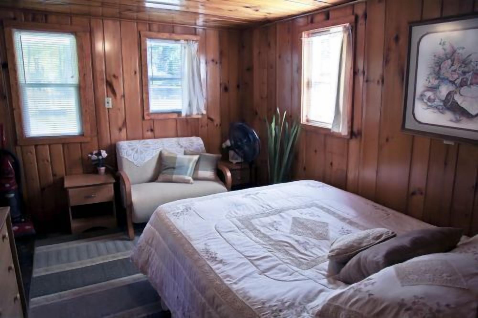 Une pièce de cabane en bois comprenant un lit, une chaise, une petite table et une fenêtre.