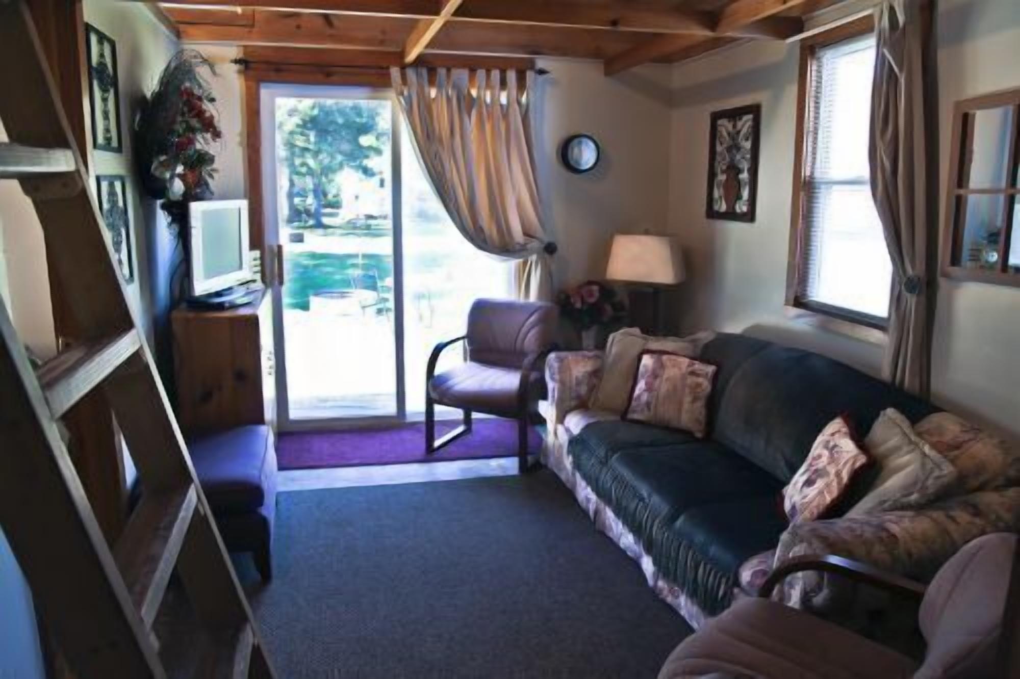 A cozy living room with a sofa, a chair, a lamp, and a television. There is a window with curtains and a door leading outside.