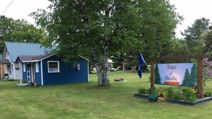 Pieni sininen talo, jossa on kuisti, ja sen edessä on kyltti, jossa lukee ”Paratiisin männyt”, sekä lippu.