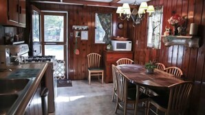 A wooden cabin interior with a kitchen, dining area, and a large window. - #4 - Loon's Landing 2 Bedroom Cabin by RedAwning (Carp Lake)