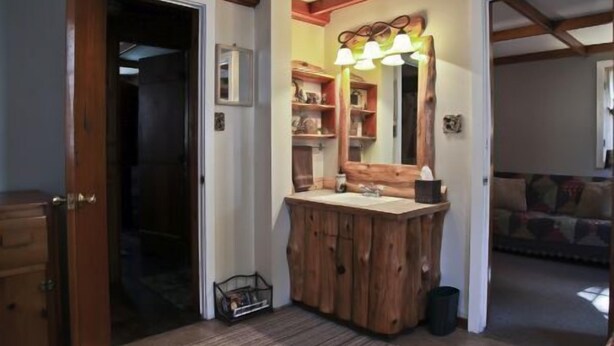A rustic bathroom with a wooden vanity, a mirror with lights, and shelves with toiletries. - #4 - Loon's Landing 2 Bedroom Cabin by RedAwning (Carp Lake)
