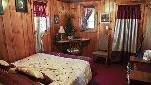 A wooden cabin room with a bed, a desk, and a chair.