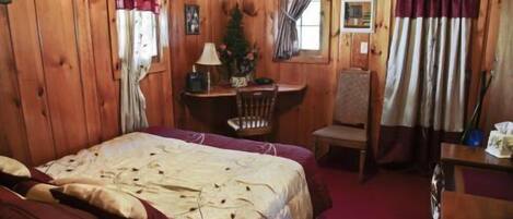 A wooden cabin room with a bed, a desk, and a chair.