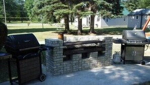 An outdoor barbecue area with a stone-built grill station, a grill cart, and a gas tank.
