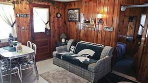 A cozy room with a plaid sofa, a dining table with chairs, a wooden door, and a small rug.