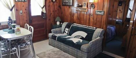 A cozy room with a plaid sofa, a dining table with chairs, a wooden door, and a small rug.