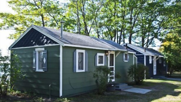 A row of small, single-story cabins with a simple, functional design, surrounded by trees.