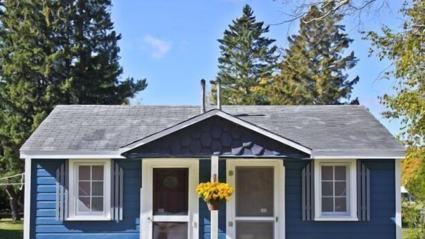 A small blue house with a porch, a white chair, and a potted plant.