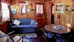 A cabin interior with a wooden interior, a blue sofa, a round table, and a staircase leading to a loft area.