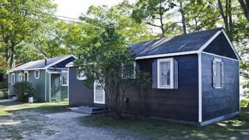 A small, single-story cabin with a dark exterior and white trim, surrounded by trees.