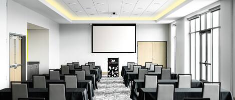 A conference room with rows of tables and chairs, a projector screen, and a large window.
