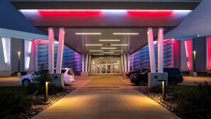 Vestíbulo moderno de edificio con paseo techado, iluminado por luces verticales y un dosel rojo.