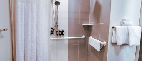 A shower area with a glass door, a handheld showerhead, a handheld showerhead, a towel rack with towels, and a shelf with toiletries.