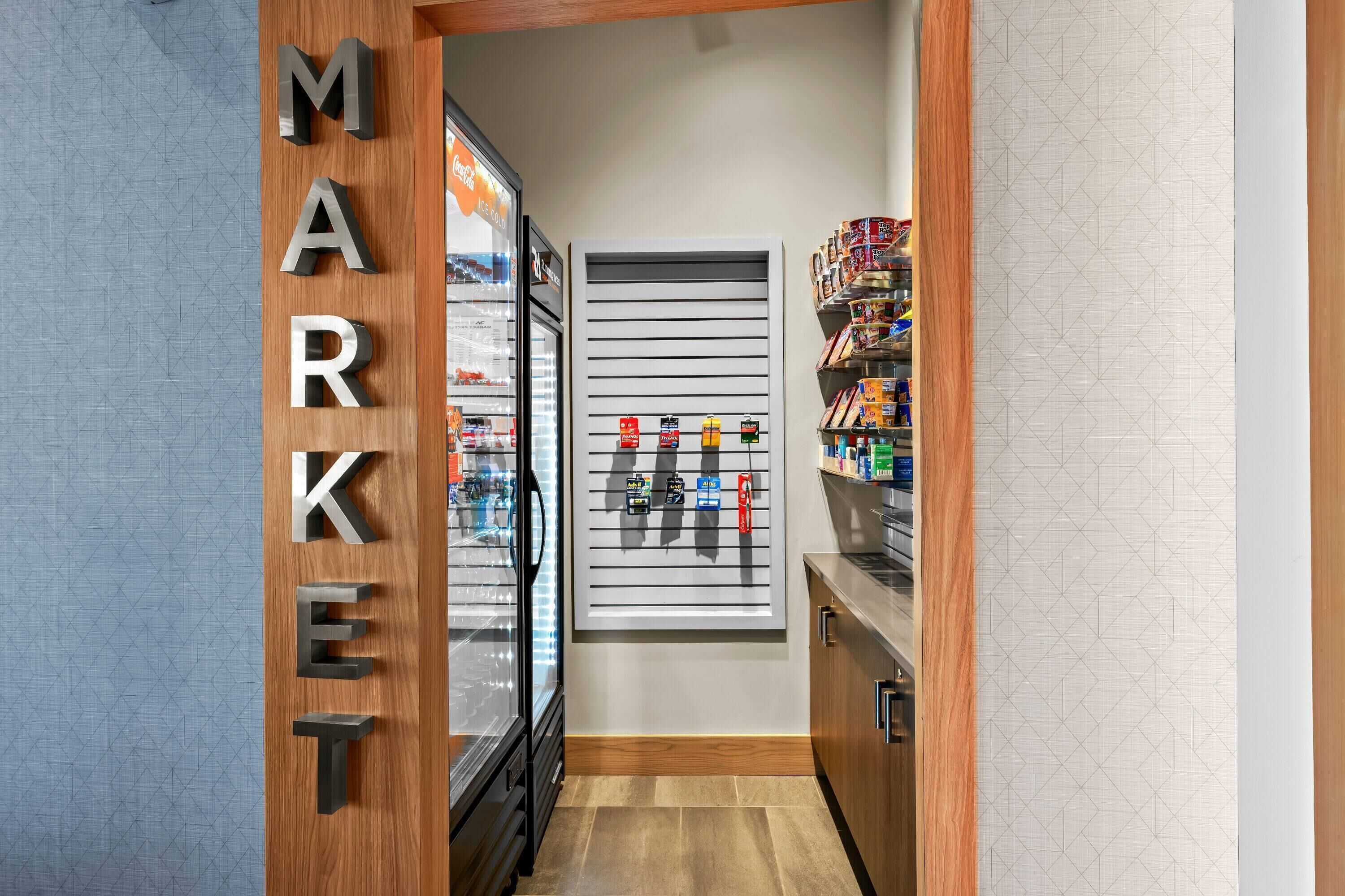 Un couloir avec un présentoir réfrigéré, un présentoir mural pour produits et des étagères remplies de produits.