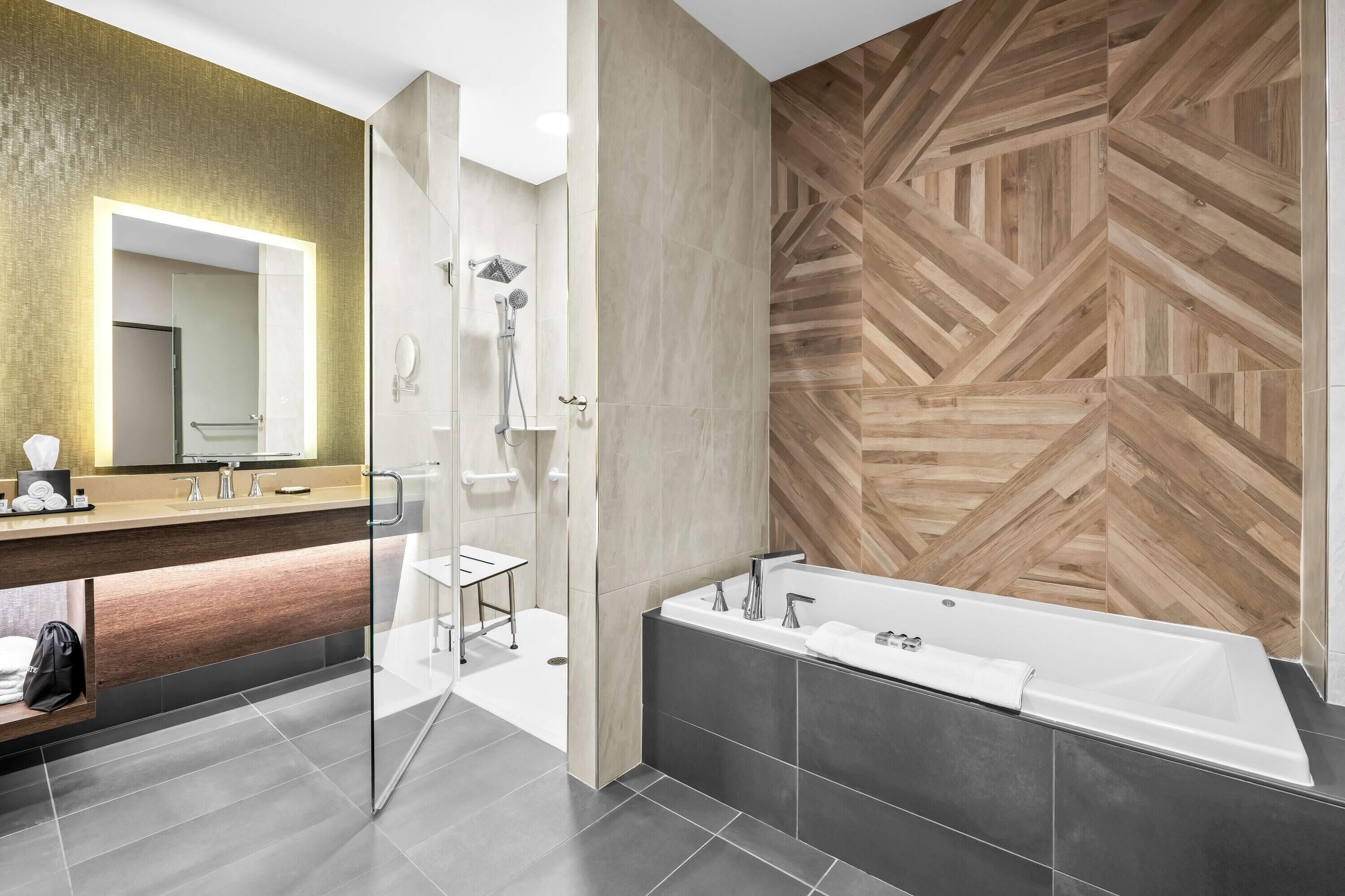A modern bathroom with a large mirror, a shower, a bathtub, and a vanity with a sink.