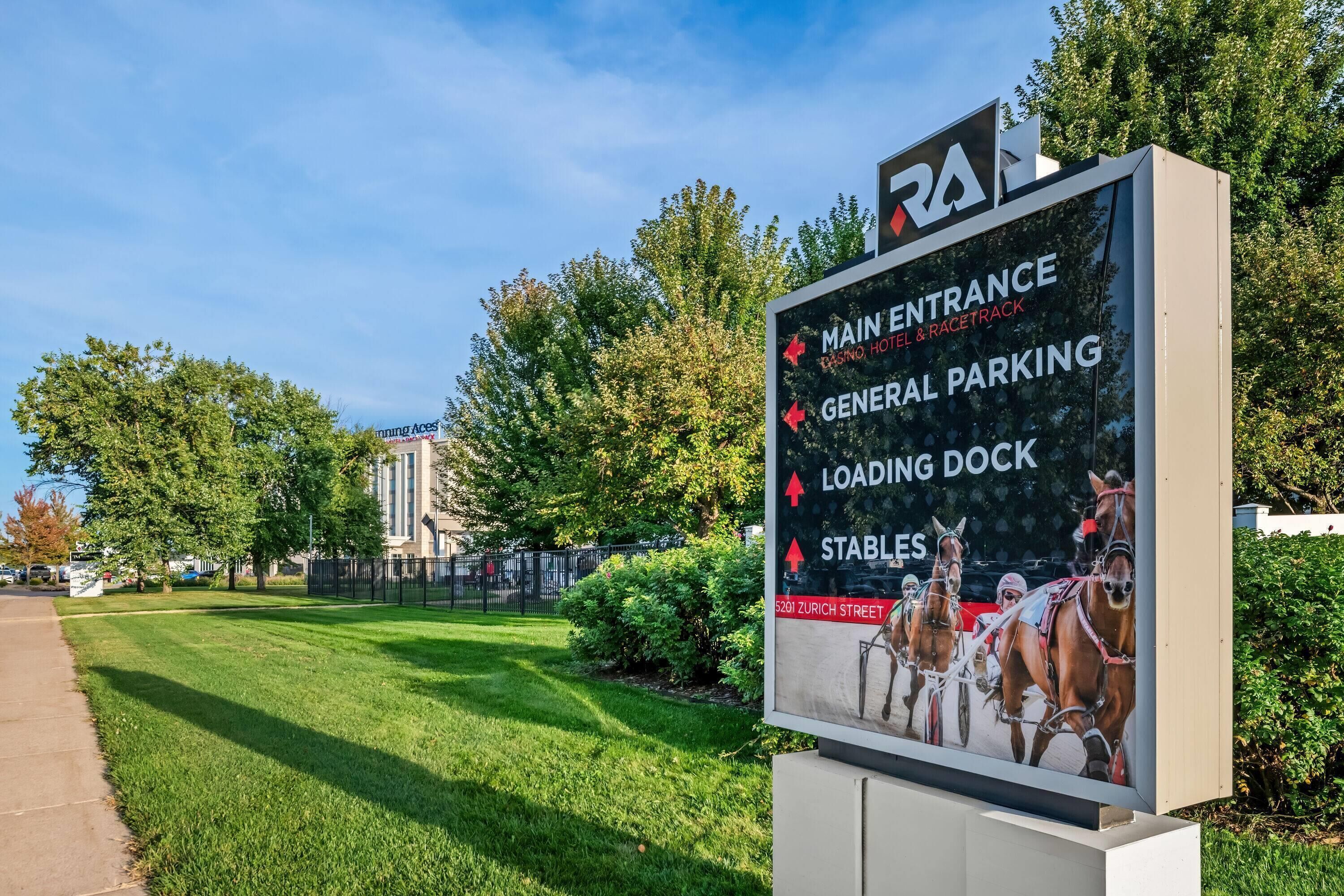 A sign indicating the main entrance to a hotel and racetrack, with general parking, a loading dock, and stables.