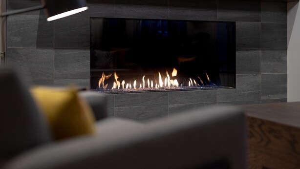 Una chimenea moderna con frente de vidrio transparente, integrada en una pared de azulejos.