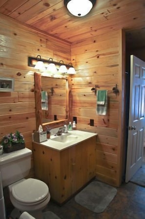 A wooden cabin bathroom with a wooden vanity, a sink, a toilet, and a mirror. - Main  - Starry Nights 2 Bedroom Cabin by RedAwning (Carp Lake)
