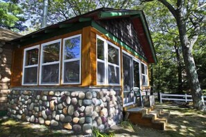 A rustic cabin with a stone foundation, large windows, and a wooden porch. - Main  - Starry Nights 2 Bedroom Cabin by RedAwning (Carp Lake)