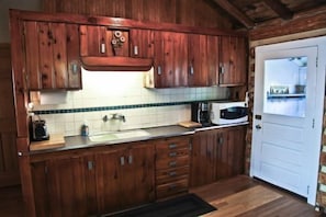 A wooden kitchen with a white door, a sink, a microwave, and a coffee maker. - Main  - Starry Nights 2 Bedroom Cabin by RedAwning (Carp Lake)