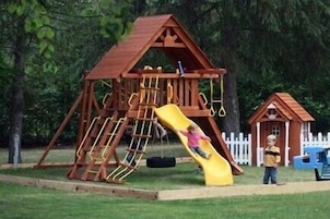 A wooden playground with a slide and swings.