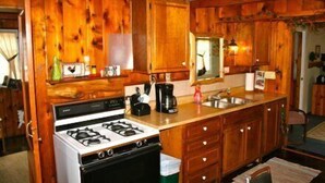 A kitchen with wooden cabinets, a stove, and a sink. - #5 - Times Square 2 Bedroom Cabin by RedAwning (Carp Lake)