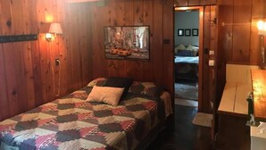 A wooden-paneled room with a bed, a wall-mounted TV, and a door leading to another room. - #5 - Times Square 2 Bedroom Cabin by RedAwning (Carp Lake)