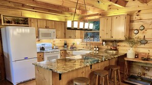 A wooden cabin kitchen with a refrigerator, stove, microwave, and bar stools. - Lake Hideaway 2 - Lakeside Log Cabin, Fishing Boat, Private Dock & Mountain View (Cherry Log)