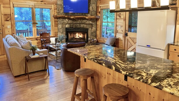 A cozy cabin interior with a stone fireplace, wooden furniture, a large TV, and a stone wall. - Lake Hideaway 2 - Lakeside Log Cabin, Fishing Boat, Private Dock & Mountain View (Cherry Log)
