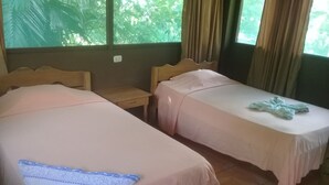 Two single beds with wooden headboards, a small bedside table, and a window with curtains. - Ecoadventure Amazon (Indiana)