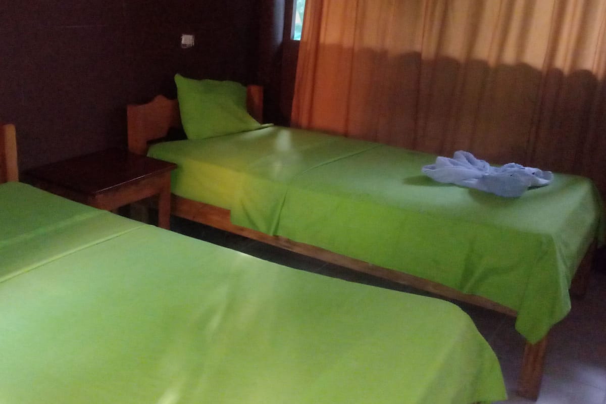 A room with two single beds, a wooden nightstand, and a small table.
