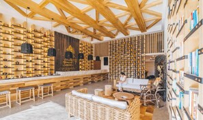 A spacious lounge area with wooden beams on the ceiling, a long bench, wicker furniture, and wall-mounted shelves with books and decorative items. - Atour S Hotel (Guangzhou)